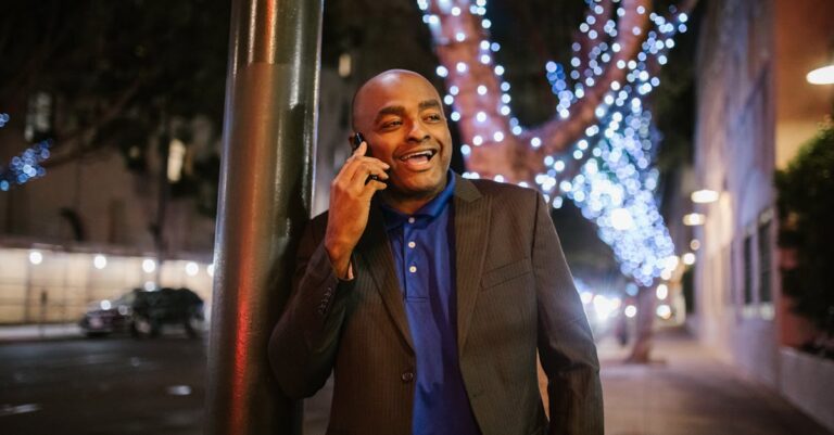 A happy man in a suit making a phone call on a decorated street at night.