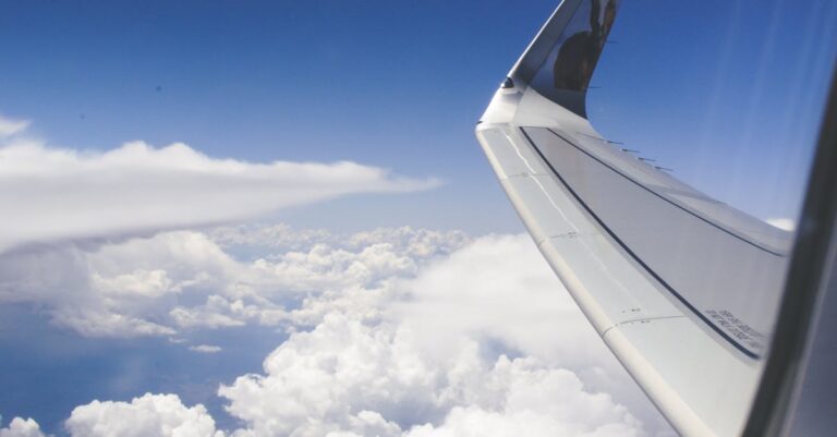 View from airplane window showcasing a wing above fluffy clouds during daylight.