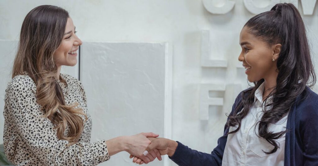 Two professional businesswomen shaking hands in a modern office setting.