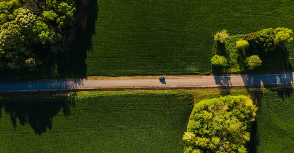 Aerial shot of a car driving on a tranquil road through lush green countryside on a sunny day.