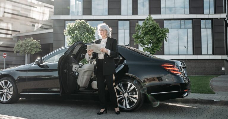 Professional adult woman in business attire reading beside a luxury car.