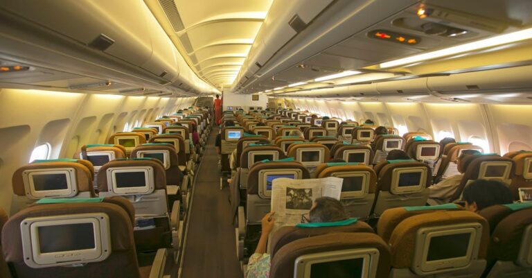 View of an airplane's cabin interior with passengers seated, highlighting in-flight entertainment.