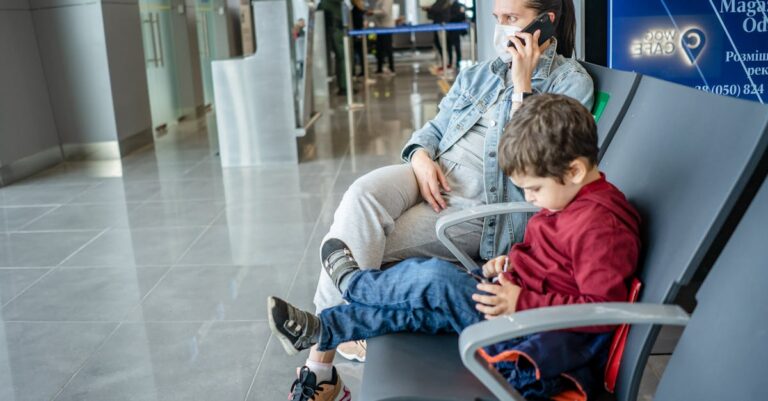 A mother and child sitting at an airport terminal. The mother is on the phone while the child is using a device.