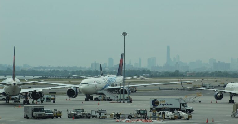 Multiple airplanes on an airport tarmac with city skyline in the background.