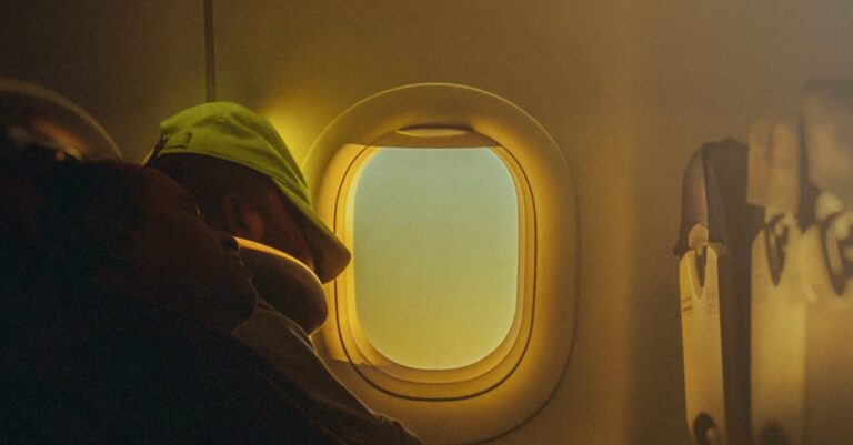 A person rests peacefully by an airplane window, warm light filtering through.