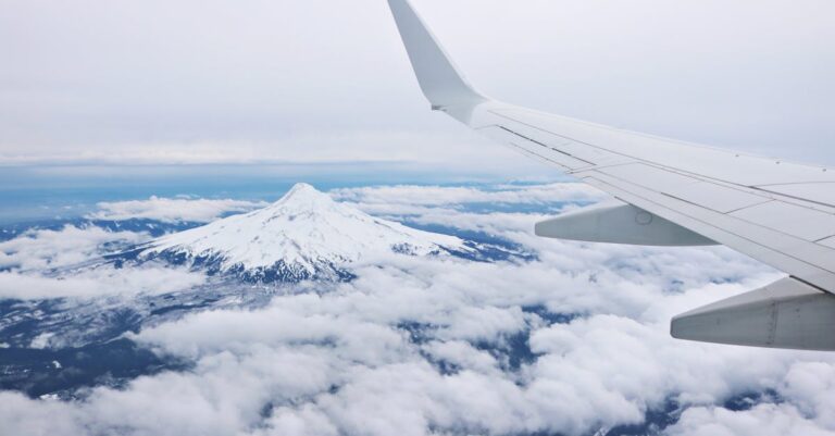 Mountain peak and airplane wing seen from above the clouds, showcasing a beautiful aerial view.