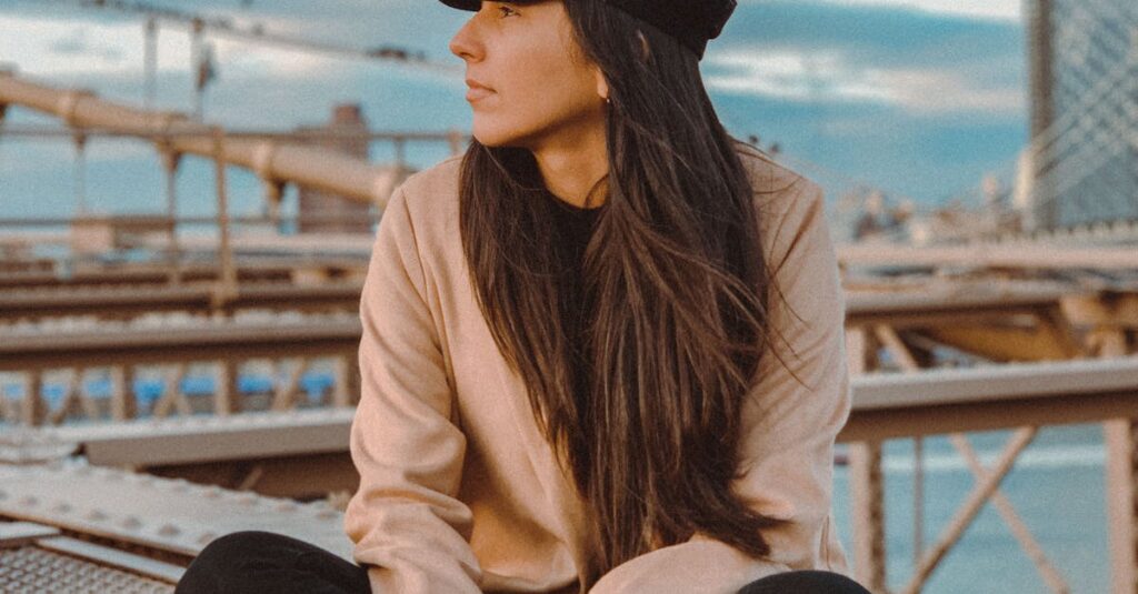 A woman in casual attire sits pensively on the Brooklyn Bridge.