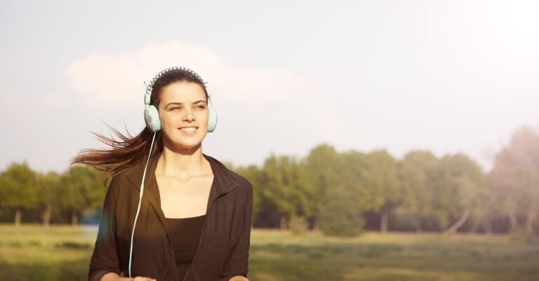 Smiling woman jogging in a park, listening to music with headphones, and enjoying the sunny day.