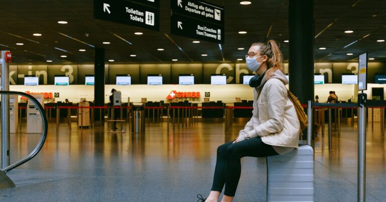 A woman wearing a face mask sits on luggage in an airport terminal amid the pandemic.