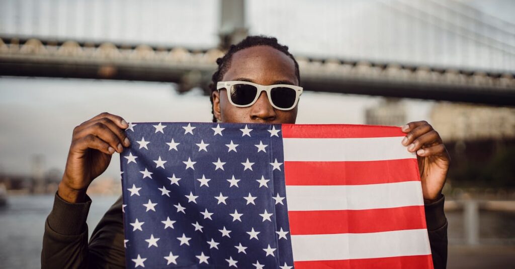 Man holding an American flag in front of a bridge in New York City, showcasing patriotism.