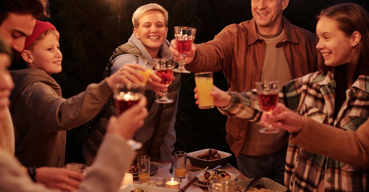 Laughing friends with kids spending time in backyard at night enjoying dinner with garlands and clinking glasses