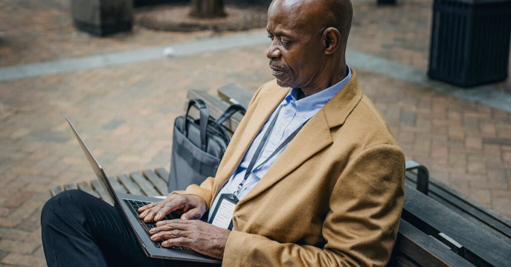 Middle-aged businessman focused on his laptop while sitting on an outdoor bench in an urban setting.