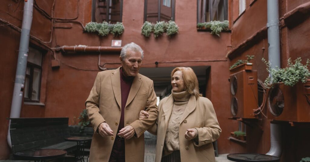 Smiling elderly couple in coats walking arm in arm through charming courtyard during winter.