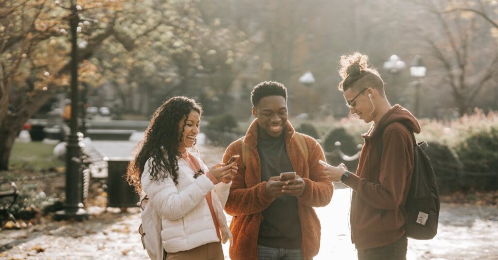 Three diverse young adults enjoying social media together in a sunny park.