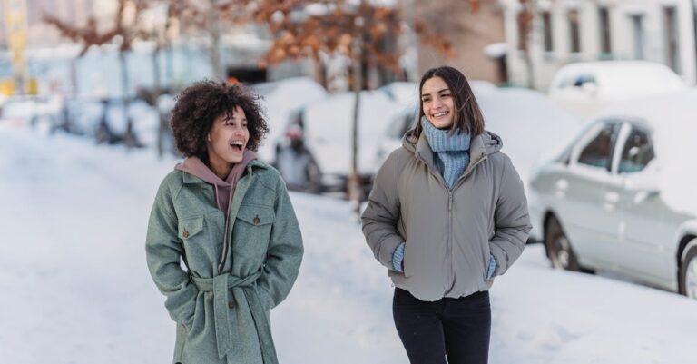 Two friends enjoying a cheerful winter walk on a snowy city street.