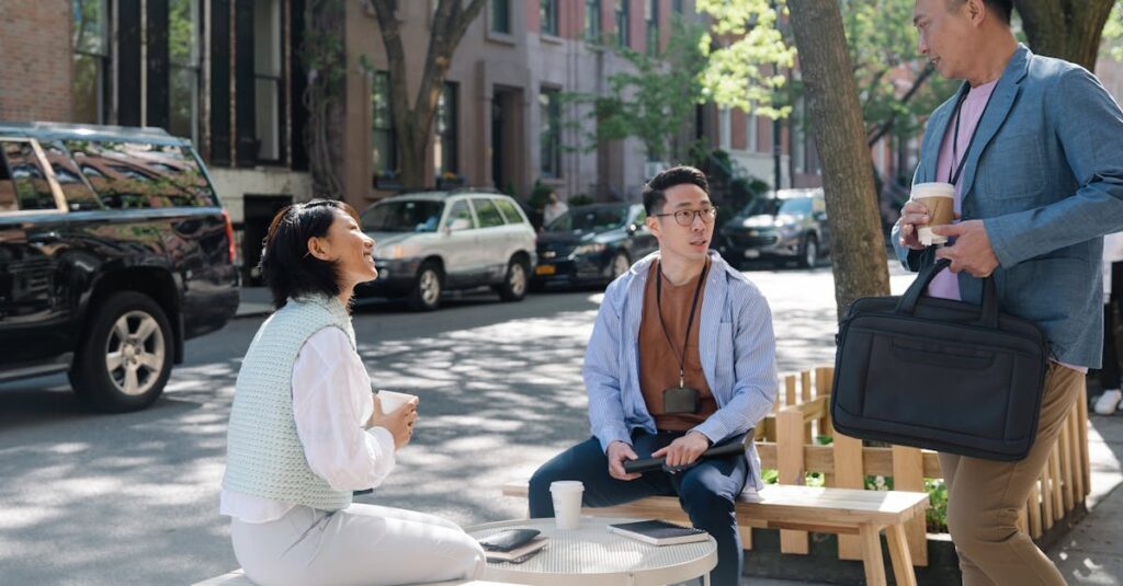 Three colleagues enjoying a coffee break on a shaded city street, engaging in conversation.