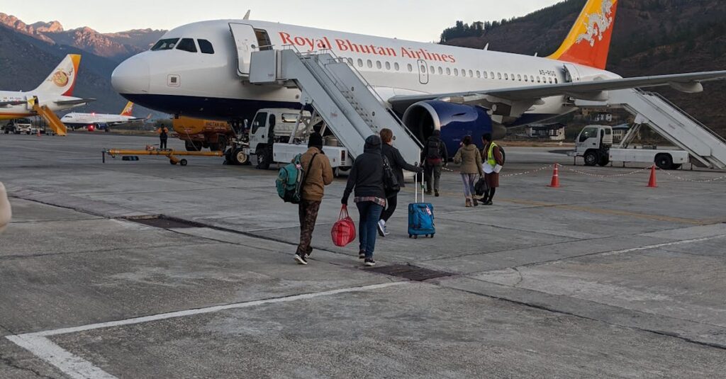 Passengers boarding a Royal Bhutan Airlines Airbus A319 at Paro Airport against mountain backdrop.