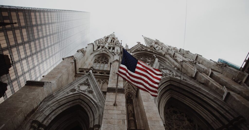 Low angle view of American flag with historic cathedral and skyscraper.