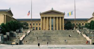 Wide view of Philadelphia Museum of Art with iconic steps and flags waving above.