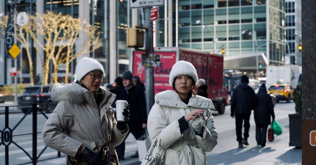 Two women in winter coats walking on a bustling city street with holiday lights.