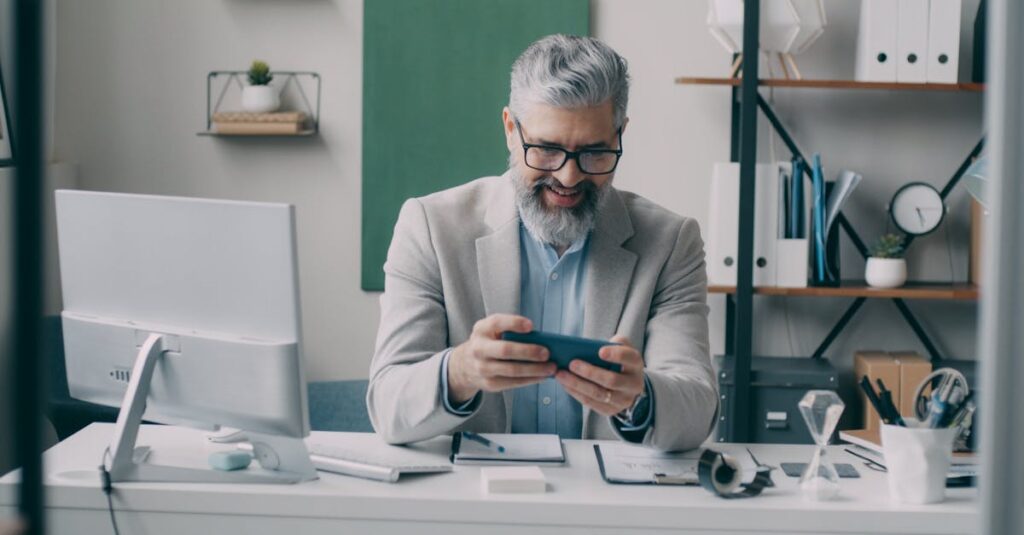 Senior businessman smiling while using smartphone at office desk.