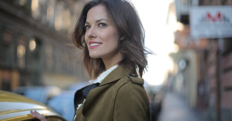 Portrait of a fashionable woman smiling beside a yellow taxi on a lively city street.