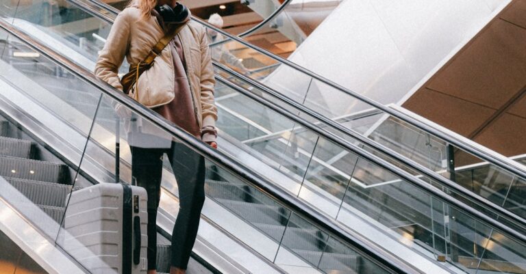 Woman with luggage wearing face mask on escalator in airport during pandemic.