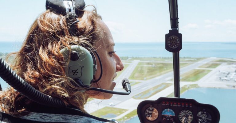 Back view of positive young female traveler in casual wear and headset sitting in cockpit of modern helicopter during flight over coastal town