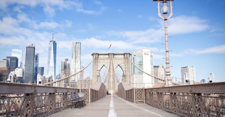 Wide-angle view of the Brooklyn Bridge leading to New York City's iconic skyline under blue skies.