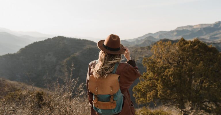 Woman wearing a backpack hiking in mountainous countryside, enjoying the scenic view.