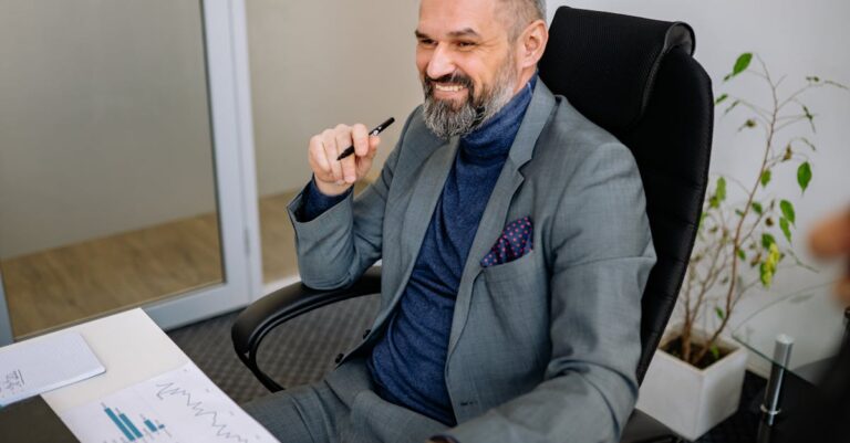 Smiling businessman in a suit sits at a desk, illustrating office professionalism.