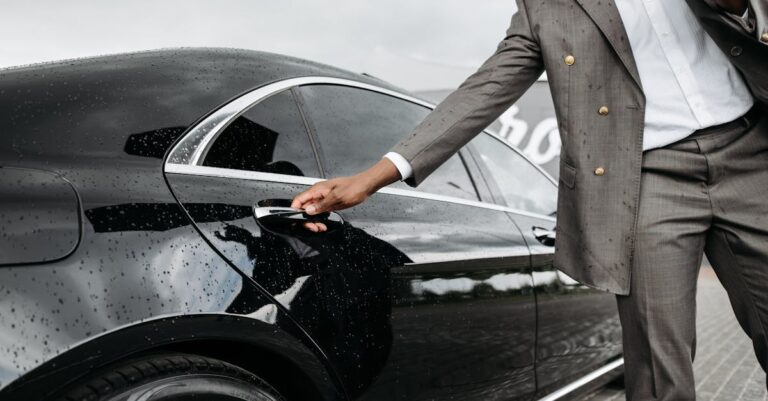 A man in a suit opens a luxury car door under raindrops on stone pavement.