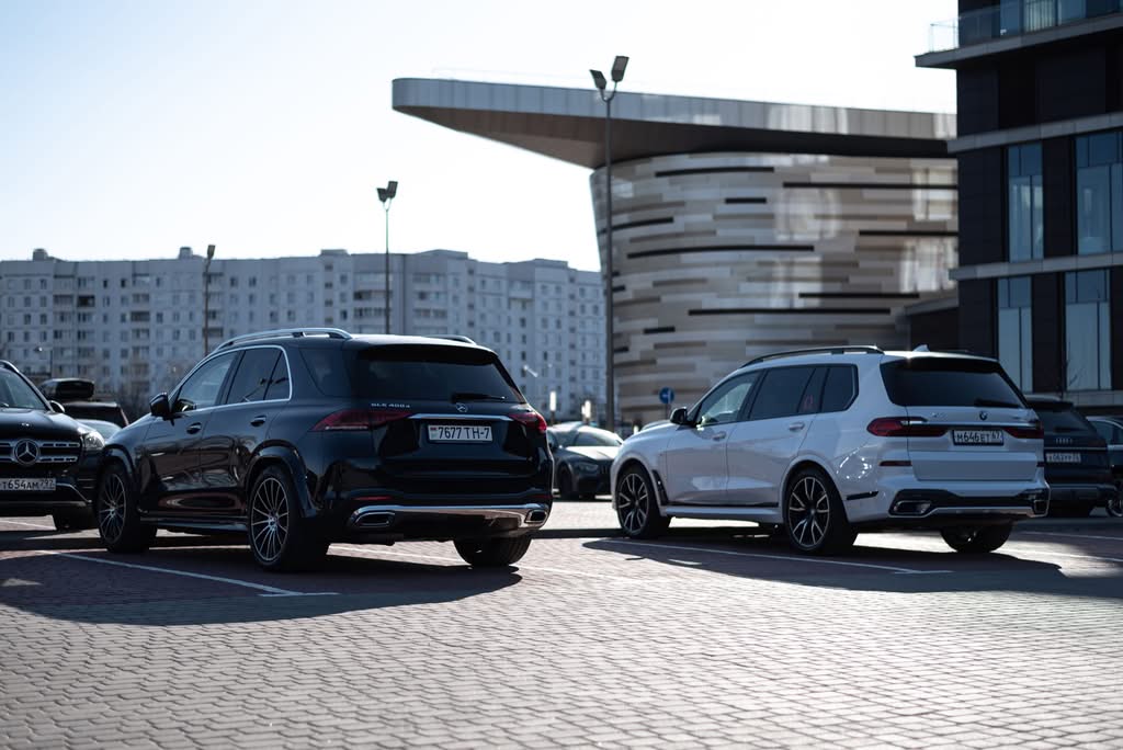 Two luxury SUVs parked in an urban setting with modern buildings in the background.