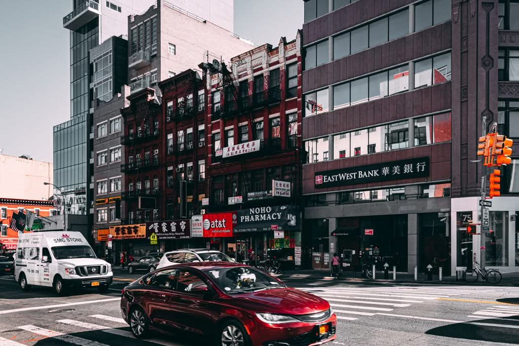 Vibrant street view of Chinatown in NYC with cars and diverse architecture under a bright sky.