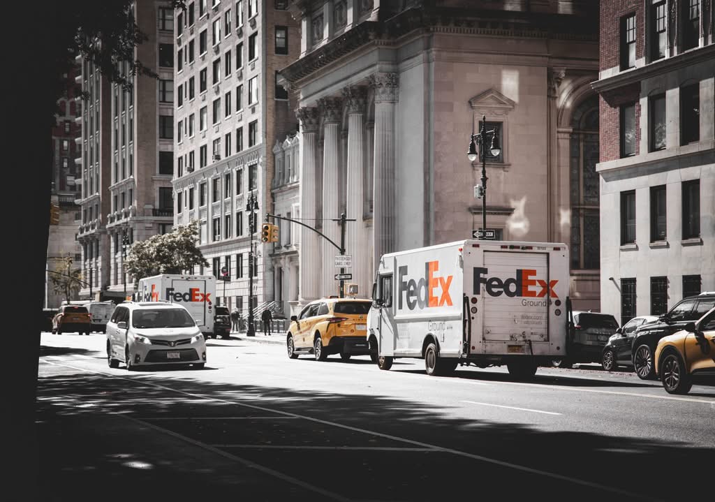 Busy street in New York City with delivery vans and cars in front of historic architecture.
