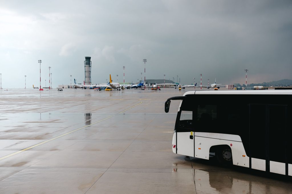 Rainy airport tarmac featuring a passenger bus with airplanes in the background.