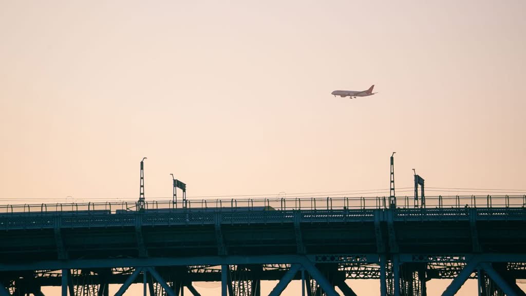 A plane flies over an urban bridge at sunset, creating a stunning silhouette.