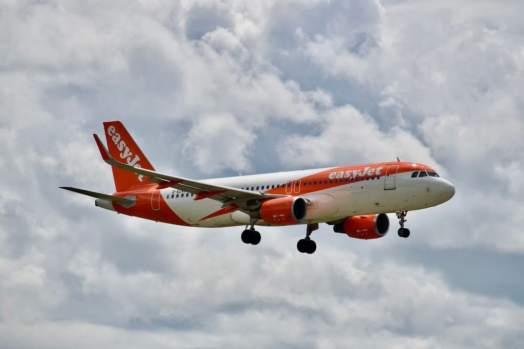 A vibrant EasyJet Airbus A320 aircraft flying amidst a cloudy sky, showcasing commercial aviation.